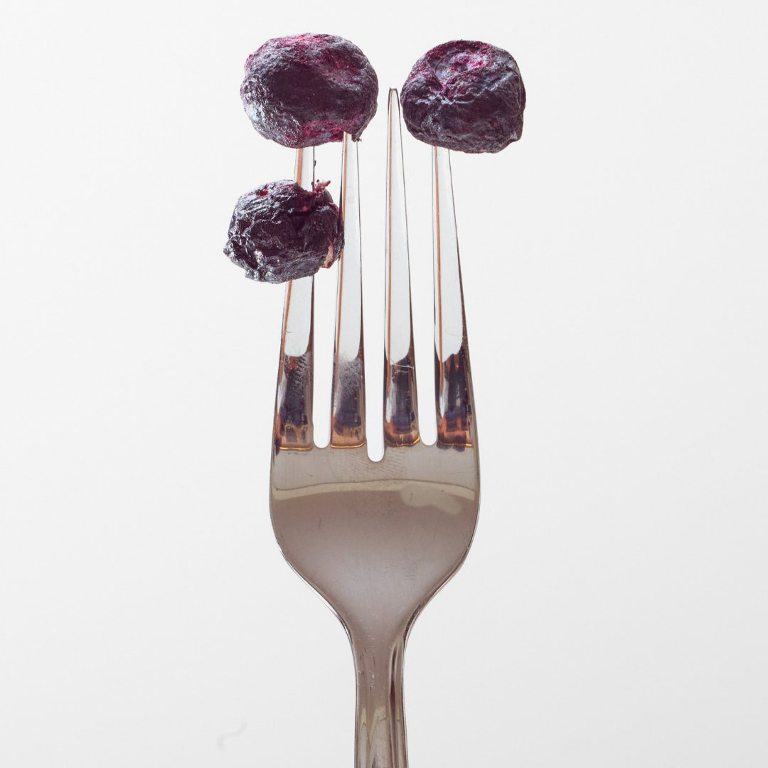 Freeze-Dried Blueberries Same Nutrients, Water Removed Three freeze-dried blueberries on the tines of a fork against a white background